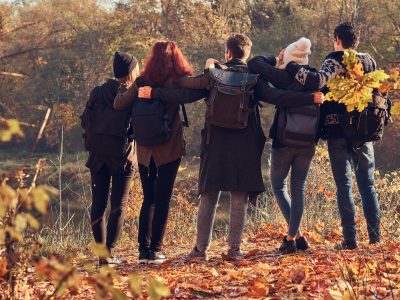 Travel, hiking, adventure concept. Back view of young friends hugging together and looking at the lake in beautiful autumn forest.